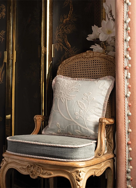Vintage-style wooden chair with embroidered cushion and curtain edged with pastel pom-pom trim by tasselora.